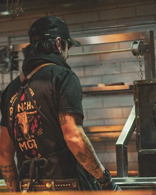 Pitmaster com o avental do Rancho MG74 em frente ao pit